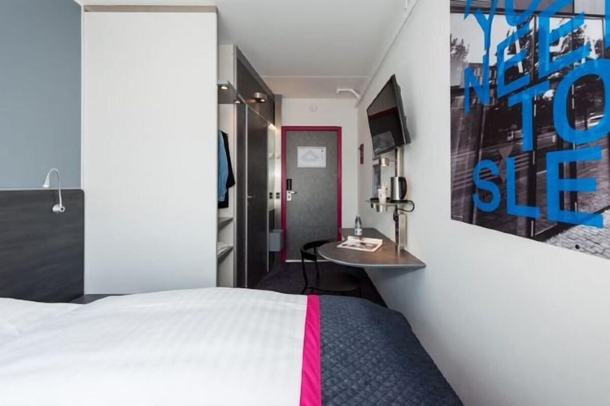 Una habitación de hotel con cama, escritorio, silla, televisor y puerta.