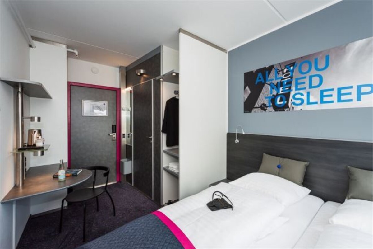 Una habitación de hotel moderna con cama, escritorio y silla. Hay un cartel en la pared y una puerta que da a un armario.