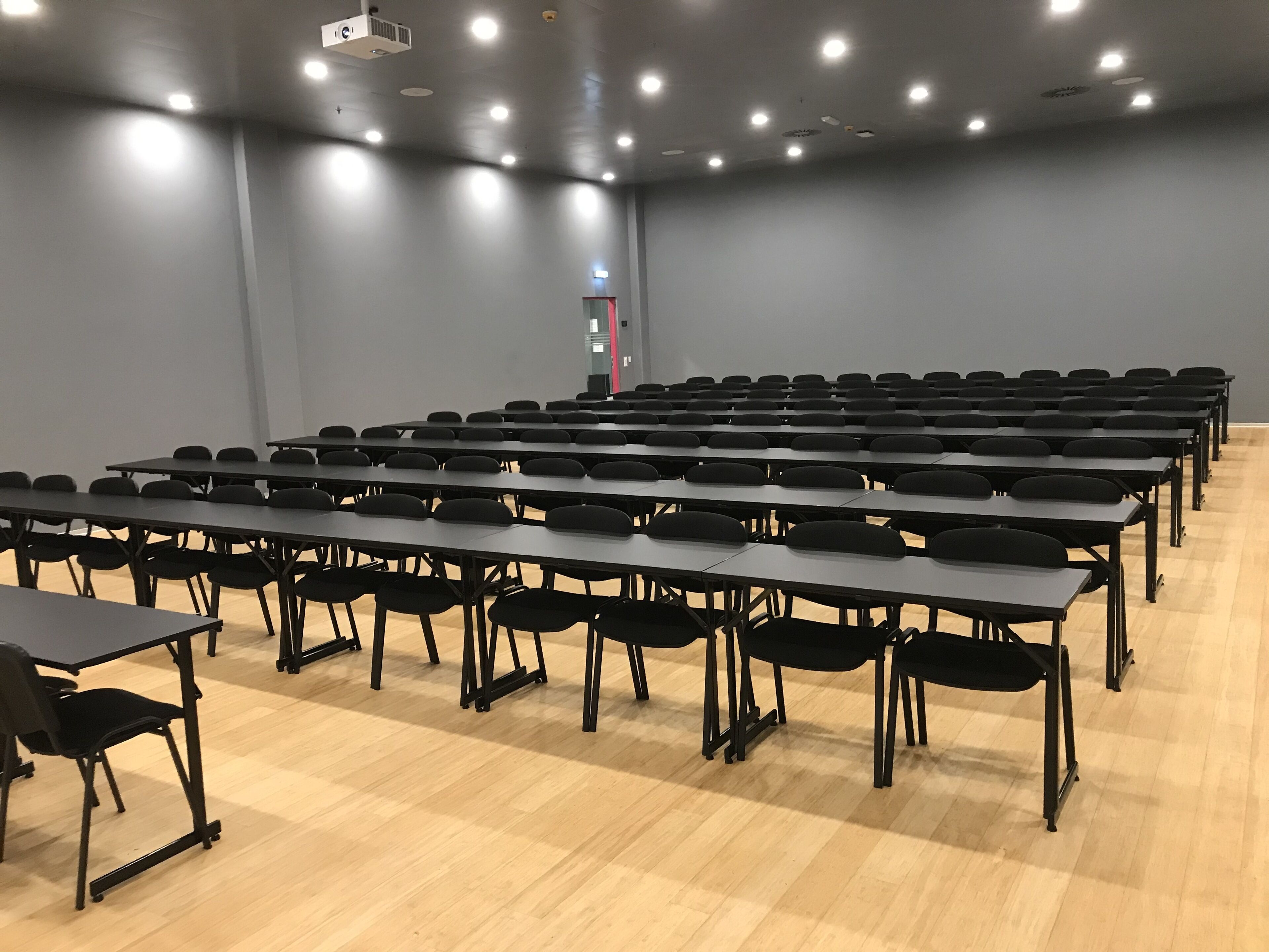 A conference room with rows of tables and chairs, a projector, and a light on the wall.