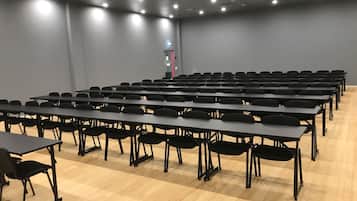 A conference room with rows of tables and chairs, a projector, and a light on the wall.