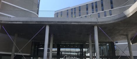 Ein modernes Gebäude mit einer geschwungenen Fassade, einem gut sichtbaren 'CABINN'-Schild und einem überdachten Eingangsbereich mit Sitzgelegenheiten.