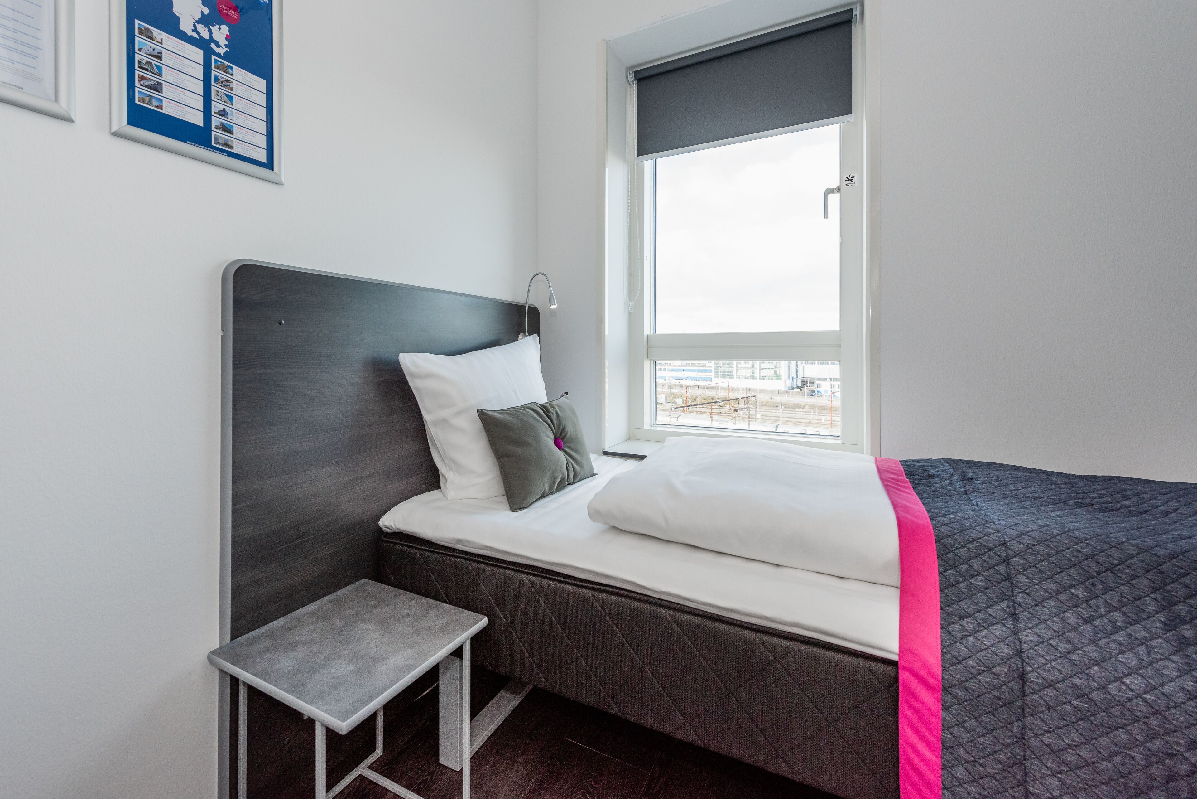 Ein modernes Hotelzimmer mit einem Bett, einem kleinen Tisch, einem Fenster mit Blick und einer gerahmten Karte an der Wand.