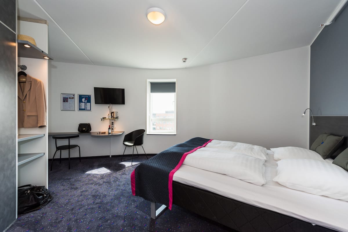 A hotel room with a bed, a desk, a chair, a wardrobe, and a television.