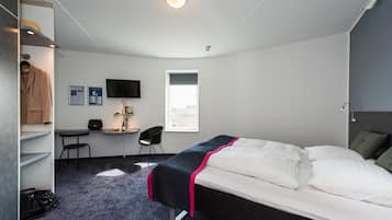 Et hotelværelse med seng, skrivebord, stol, garderobeskab, fjernsyn og et vindue.