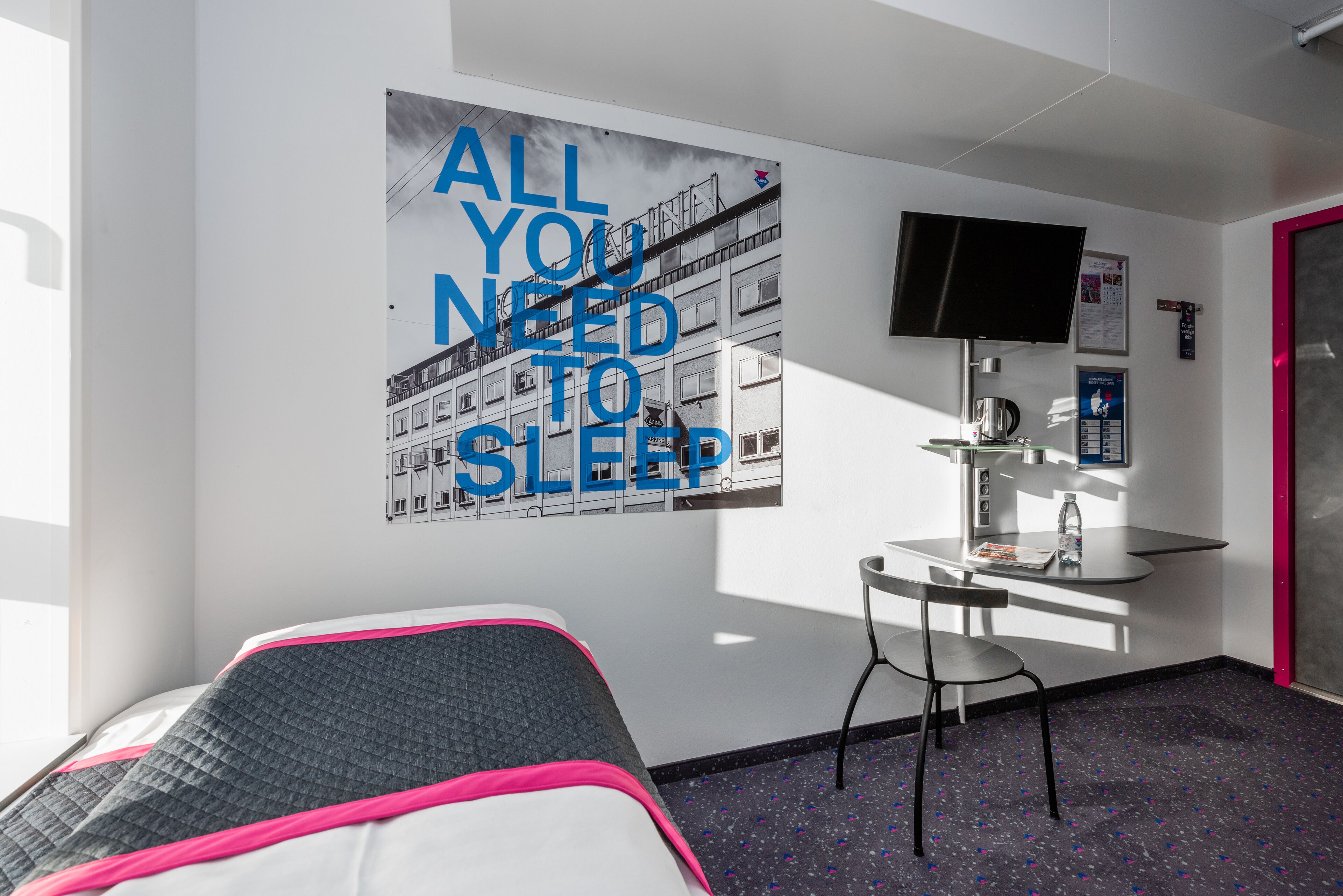 Ein Hotelzimmer mit Bett, Schreibtisch, Sessel, Fernseher und einem Bild an der Wand.