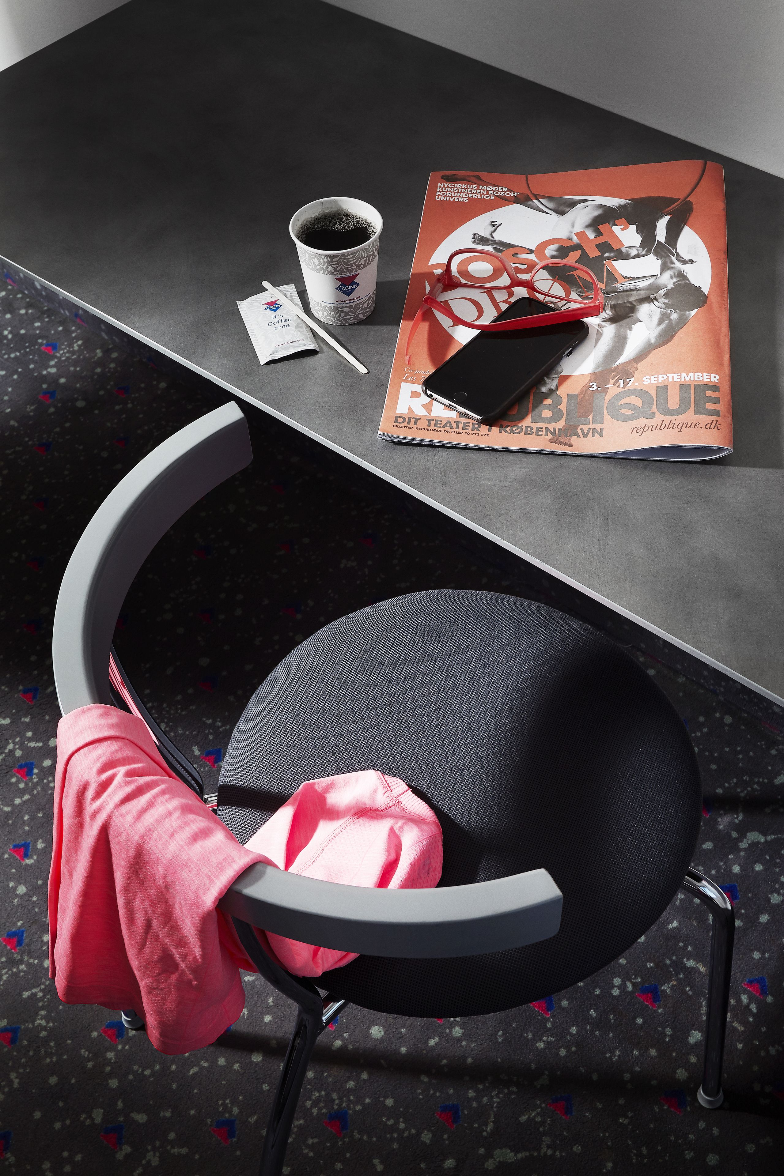 Una silla con una toalla rosa, una revista, una taza de café y un teléfono inteligente sobre una mesa.