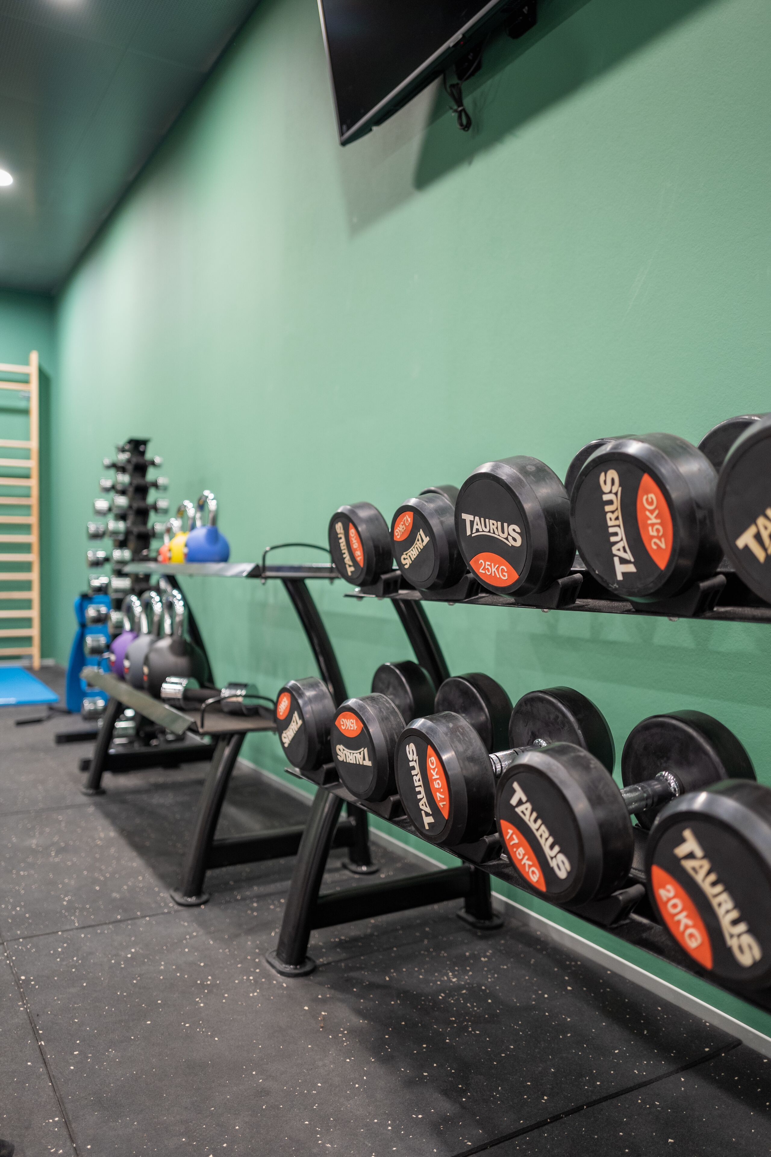 A gym with dumbbells labeled 'TAURUS' and weights on racks.