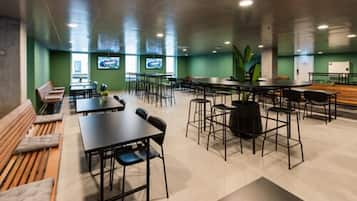 Un espacio interior amplio con varias mesas y sillas, un banco largo y una planta grande.