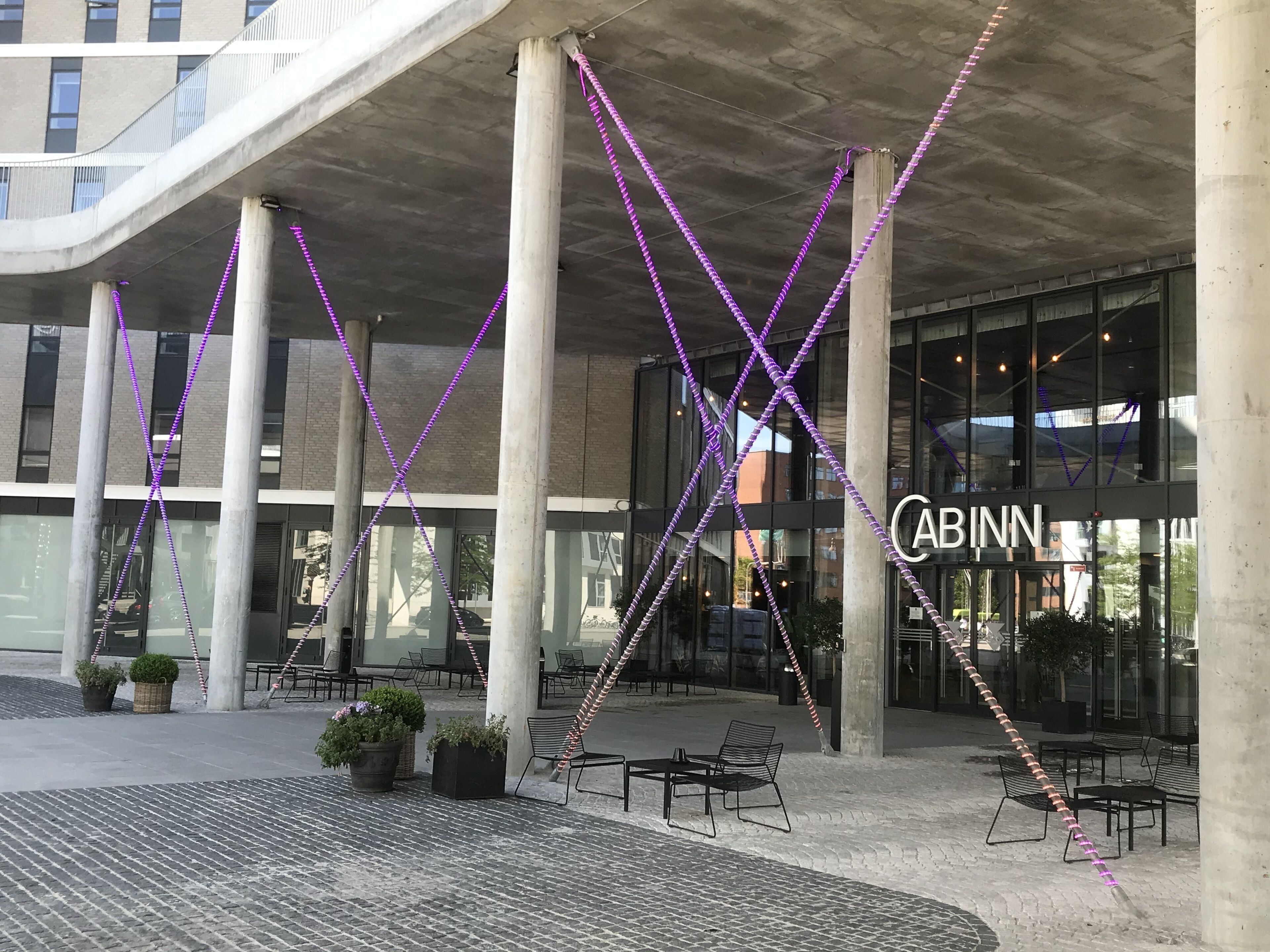 A modern building with a glass facade, outdoor seating area, and a visible 'CABINN' sign.
