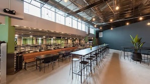 Una amplia cafetería con mesas largas y techos altos, con iluminación de estilo industrial y ventanas grandes.