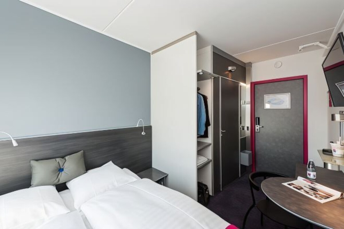 Una habitación de hotel con cama, escritorio, silla, armario y puerta.