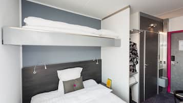 Habitación de hotel con literas, una mesita de noche con un libro, zona de ducha y baño con espejo y toallero.