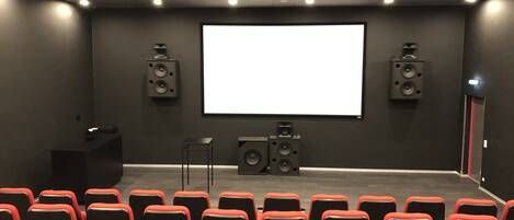 Un teatro con hileras de asientos rojos y negros, una pantalla grande y altavoces a ambos lados.