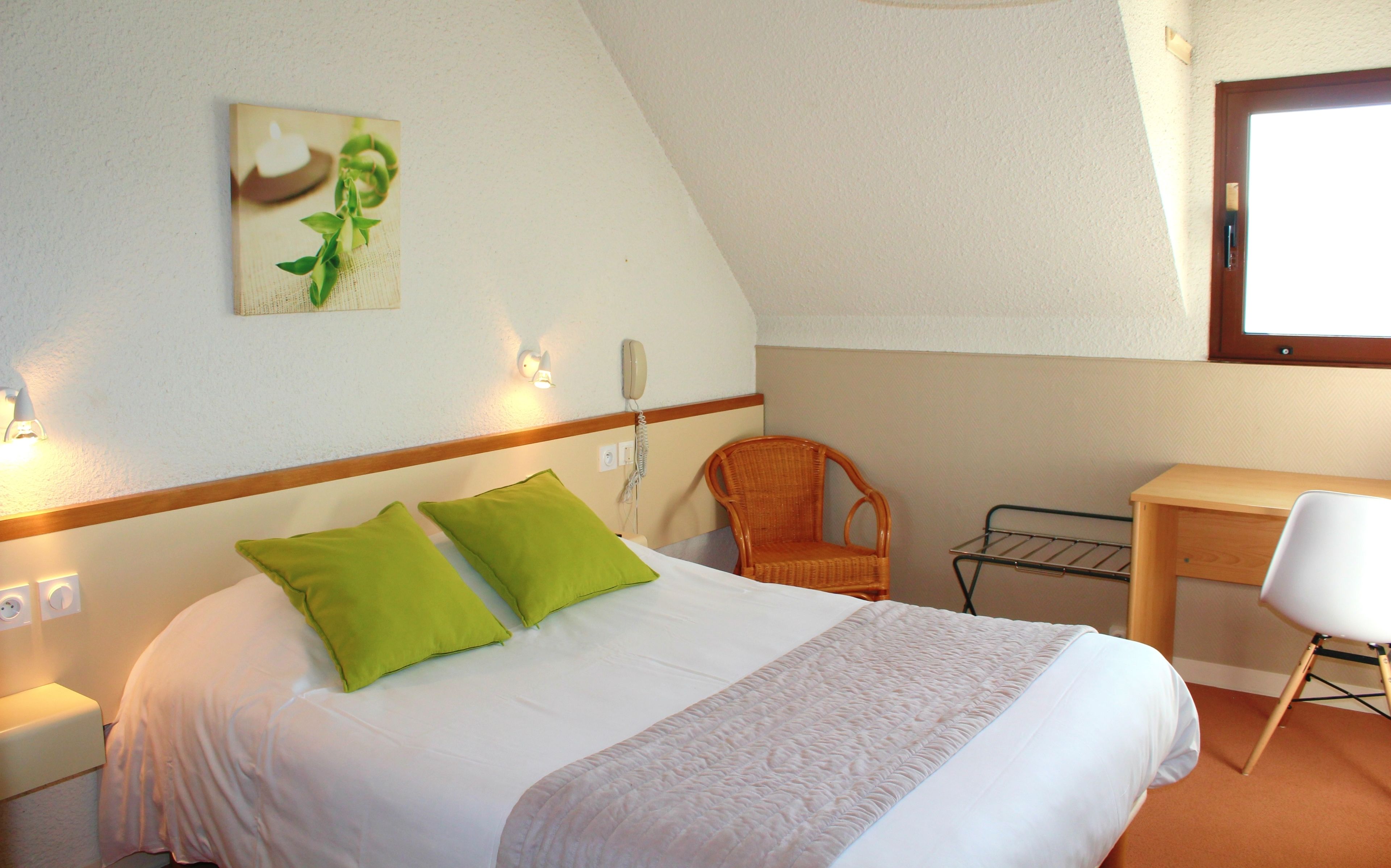 A bedroom with a bed, a chair, a desk, a wall-mounted phone, and a window.
