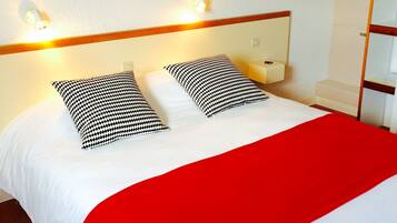 A neatly made bed with a red throw blanket and two black and white patterned pillows.