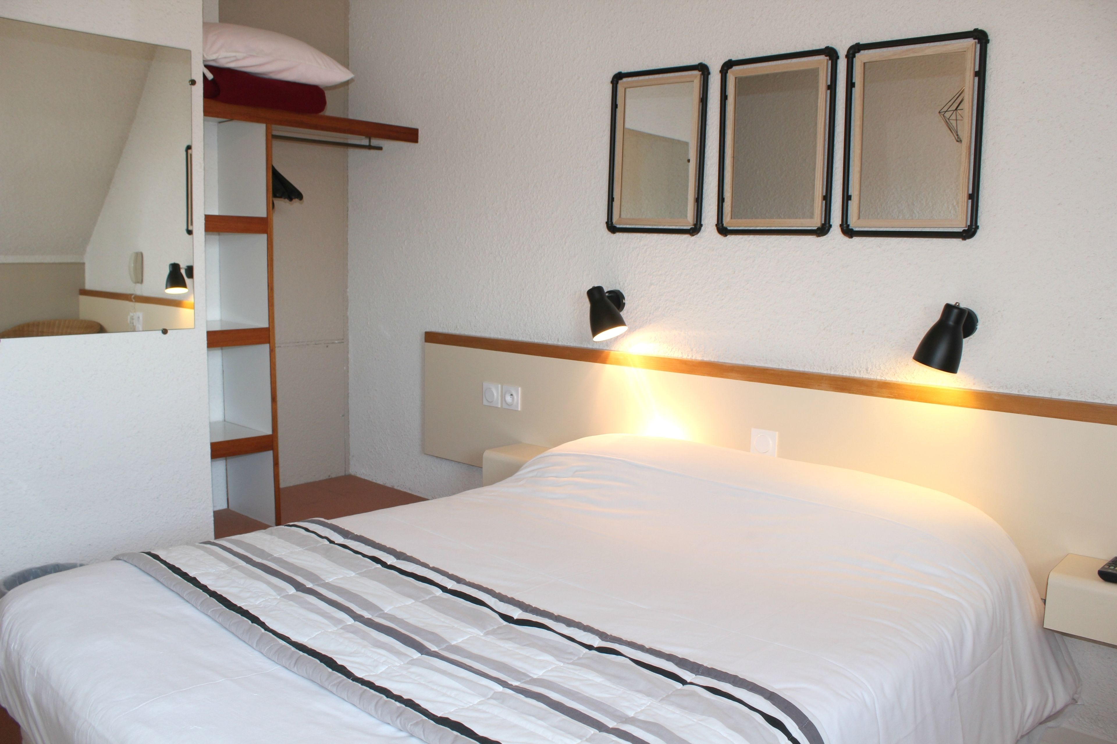 Une chambre à coucher avec un lit, des lampes de chevet, une étagère avec un miroir et une armoire.