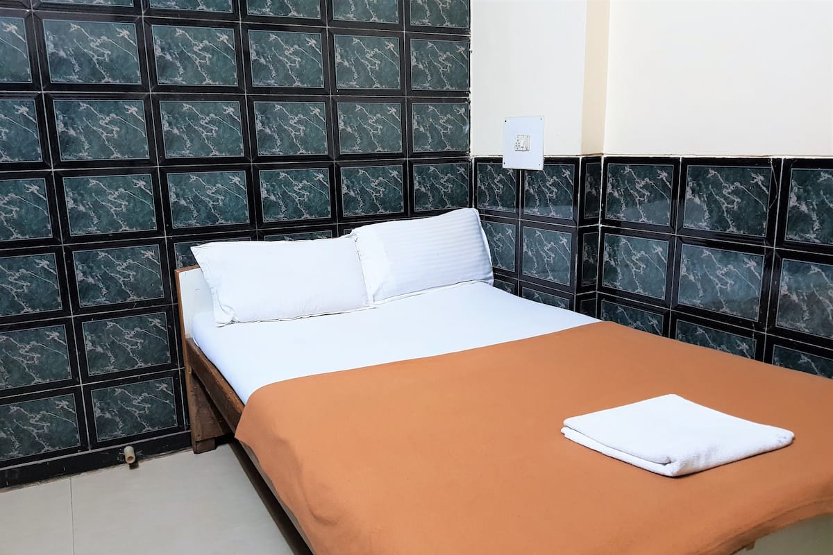 A single bed with a white mattress and brown blanket, against a wall with a dark, marble-like pattern.