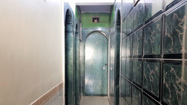 A narrow hallway with tiled walls and a tiled floor, leading to a door with a number plate. - Hexa Metro Plaza (Mumbai)