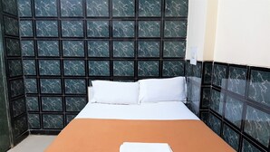 A small, neatly made bed with white linens and a brown blanket, set against a wall with a geometric pattern of dark and light tiles. - Hexa Metro Plaza (Mumbai)
