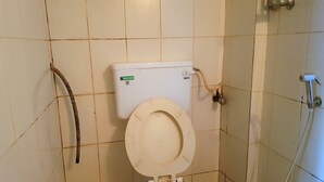A toilet with a white seat and tank, a visible flush handle, and a water hose on the wall. - Hexa Metro Plaza (Mumbai)