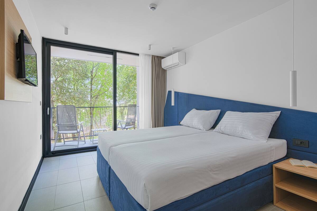 A hotel room with a large bed, a balcony with chairs, and a TV mounted on the wall.