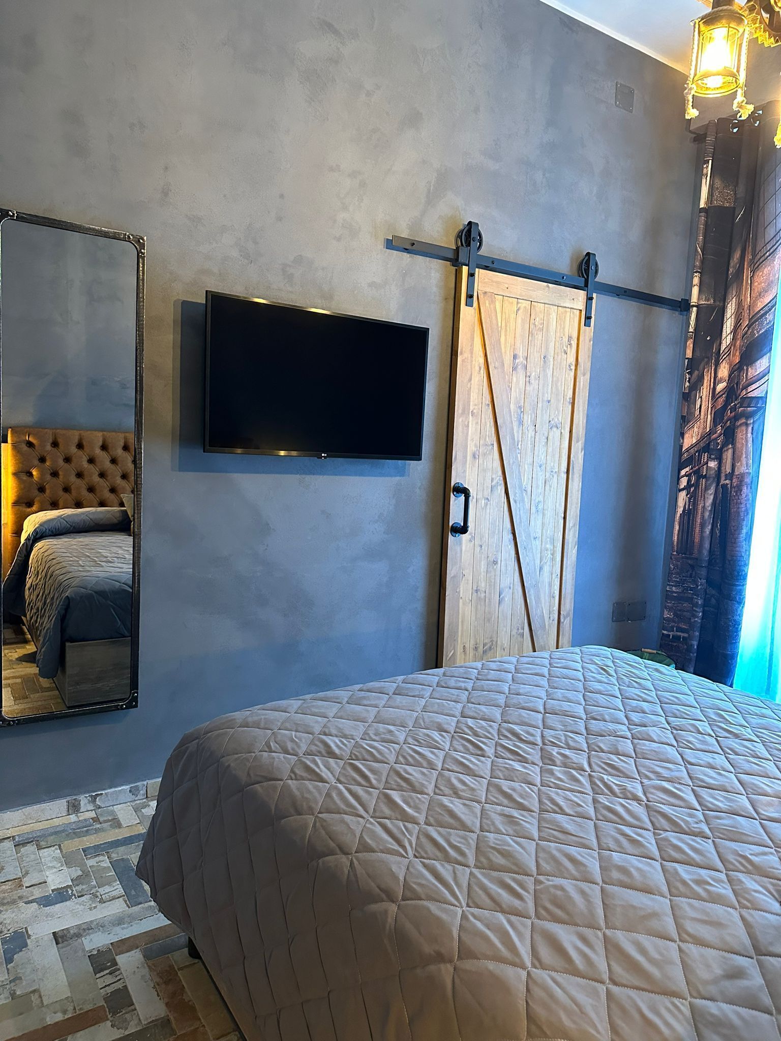 Un dormitorio con una cama grande, un televisor montado en la pared, una puerta corrediza estilo granero y un espejo que refleja la cama.