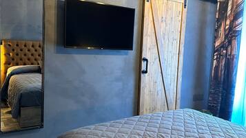 Un dormitorio con una cama grande, un televisor montado en la pared, una puerta corrediza estilo granero y un espejo que refleja la cama.