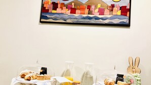 Una mesa con pasteles, una jarrón de leche y una pintura de un paisaje urbano.