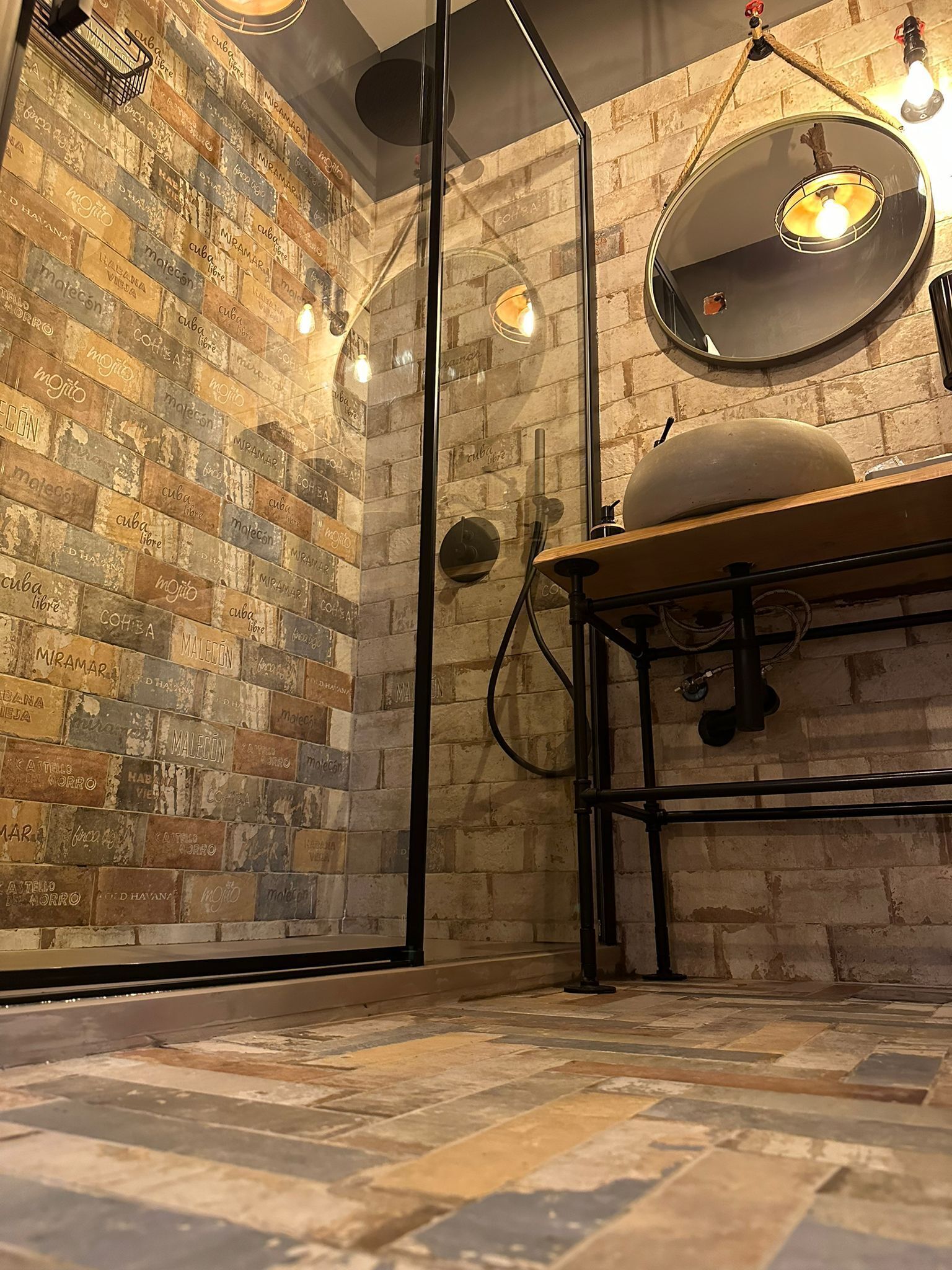 A room with a brick wall, a round mirror, and a wooden table.