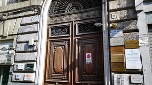 Un edificio histórico con una gran puerta doble de madera, detalles de metal ornamental y varios letreros de negocios.