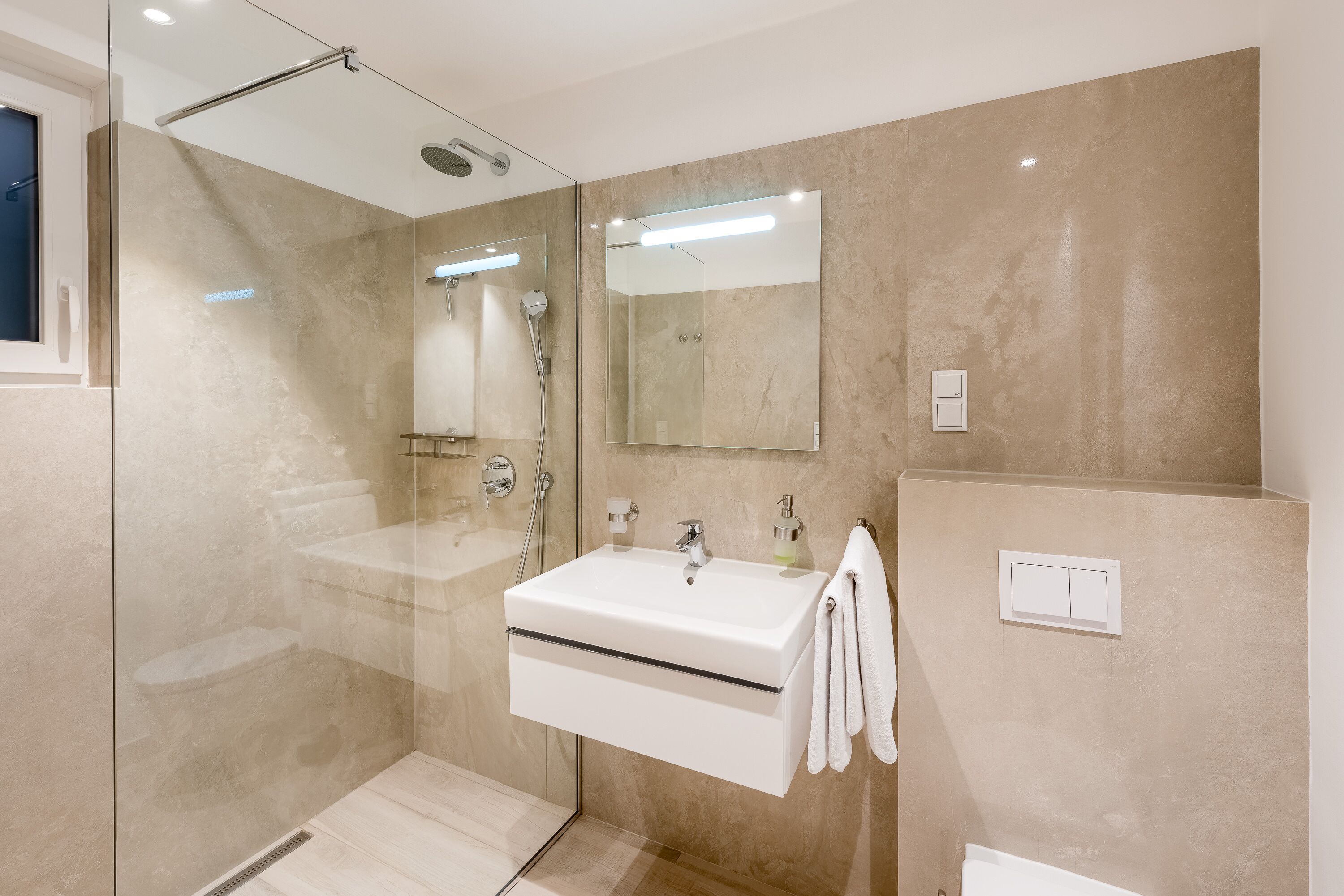 Une salle de bain moderne avec une douche à parois de verre, un lavabo blanc et un grand miroir.