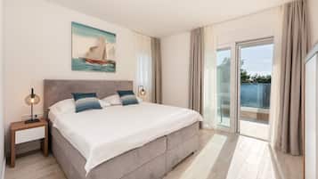 A spacious bedroom with a large bed, a nightstand, a painting of a sailboat, and a balcony with curtains.