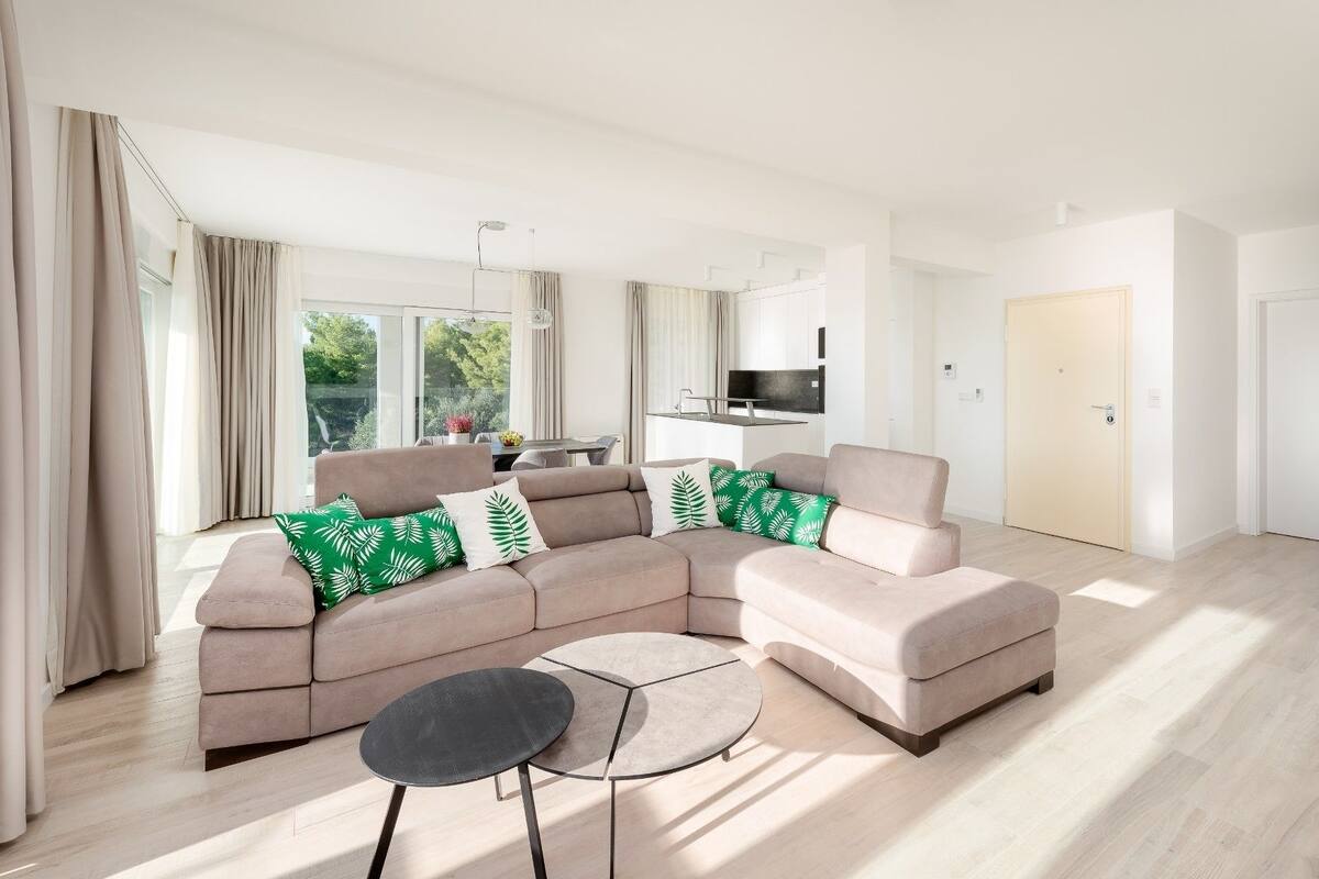 Een moderne woonkamer met een grote hoekbank, een ronde salontafel, en een eethoek op de achtergrond.