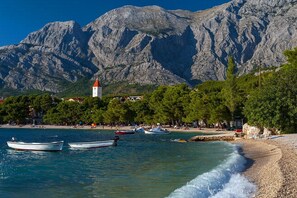 A coastal scene with boats, a beach, and a mountain backdrop.