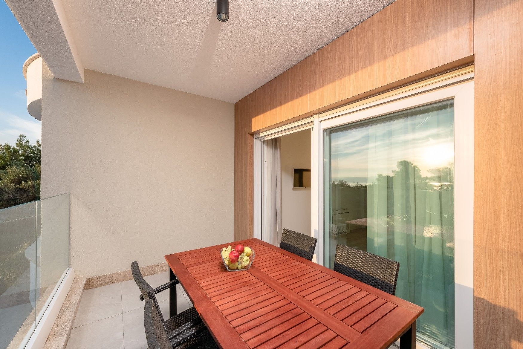 A balcony with a wooden table and chairs, a glass door, and a view of the surrounding landscape.