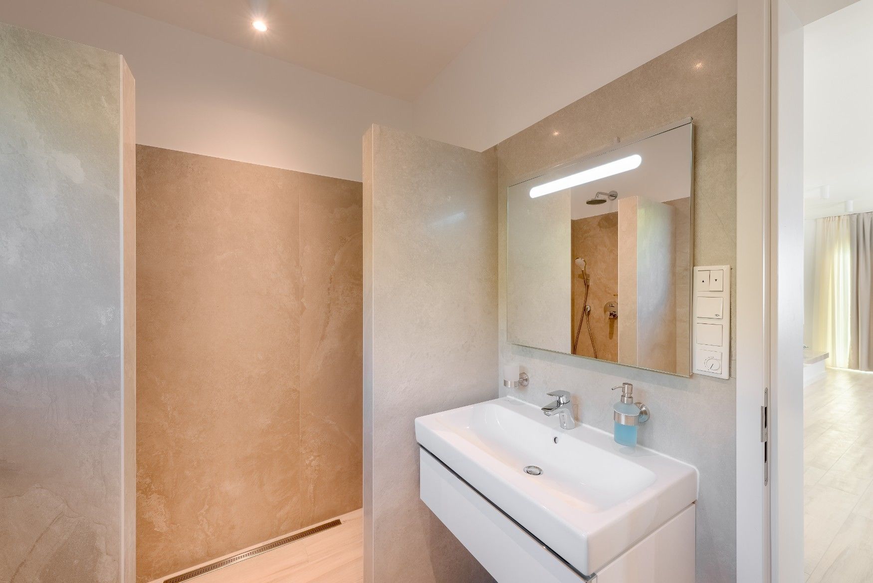 A modern bathroom with a large mirror, a white sink, and a shower area.