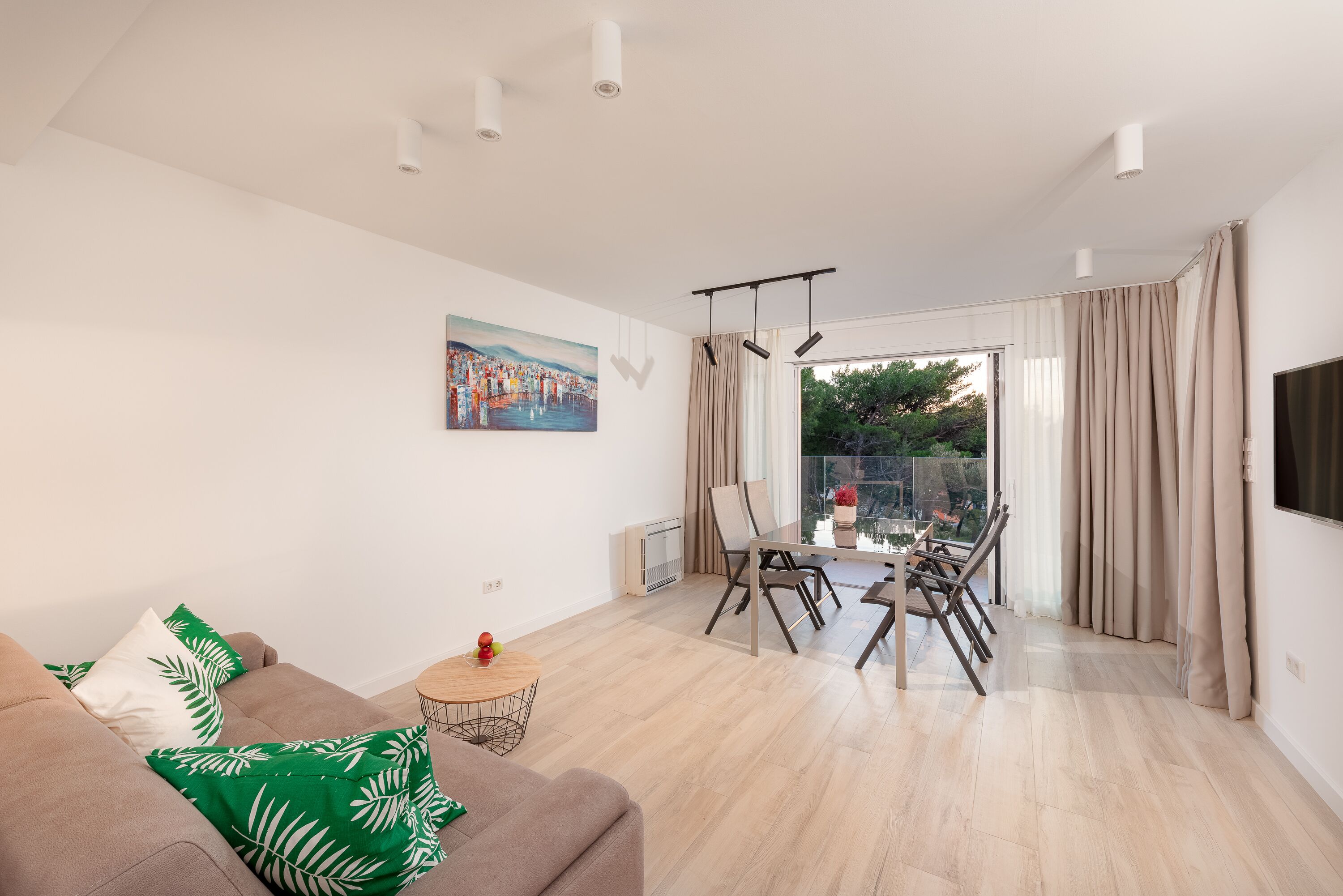 A modern living room with a sofa, a dining table with chairs, a painting on the wall, and a view through the window.