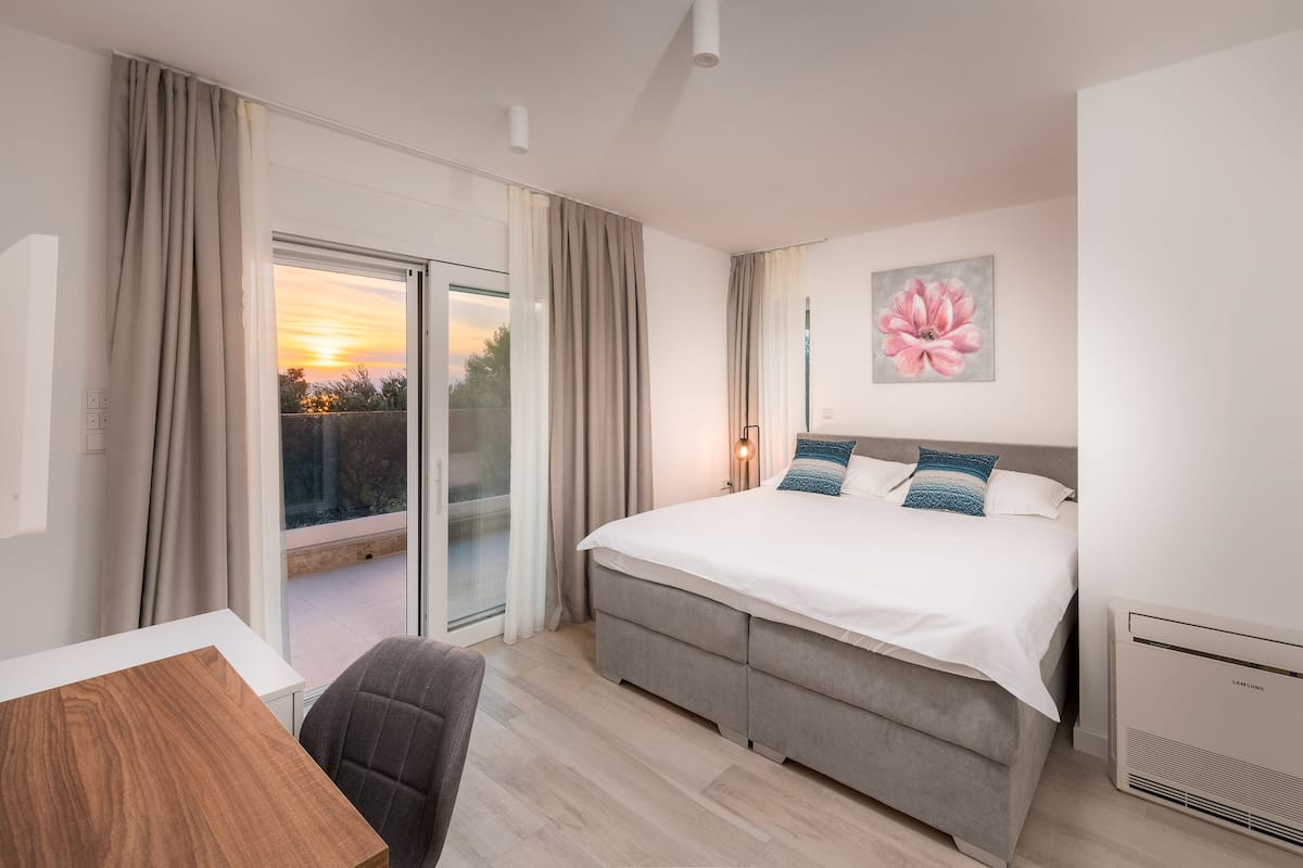 Een moderne hotelkamer met een groot bed, een bureau en uitzicht op de ondergaande zon door de schuifglazen deur.