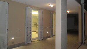 A hallway with three doors, each with a light fixture above. The doors are open, revealing a kitchen area with cabinets and a countertop. The hallway has a tiled floor and walls painted in a light color. - Frem SGV between Chianti Florence and Arezzo (San Giovanni Valdarno)