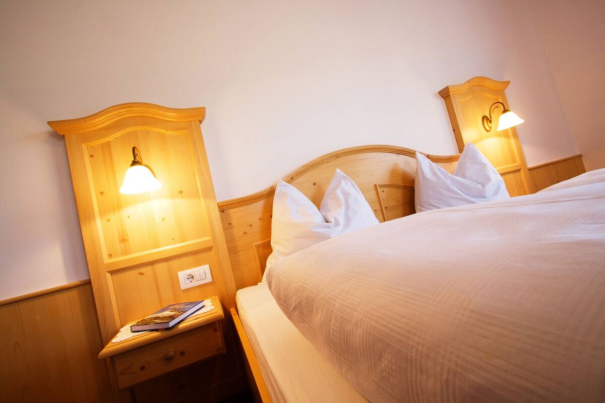 A neatly made bed with white linens, wooden headboard, and bedside lamps.
