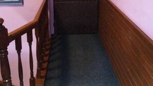 Ein Flur mit einer Holztreppe, einer mit Nummern gekennzeichneten Tür und einem Landschaftsbild an der Wand.
