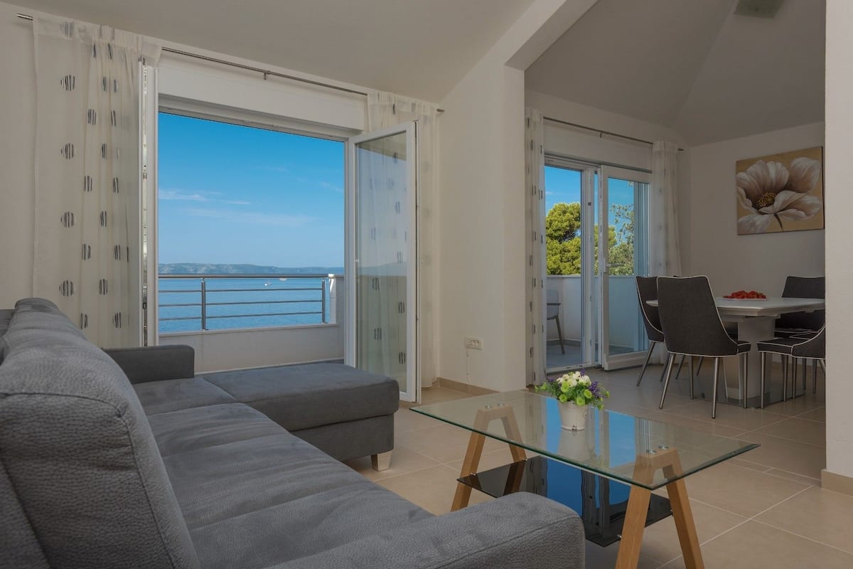 A modern living room with a grey sofa, a glass coffee table, and a dining area with a table and chairs.