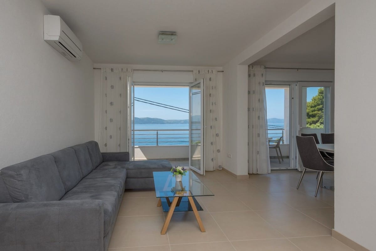 A modern living room with a grey sofa, a small coffee table, and a view of the sea through large windows.
