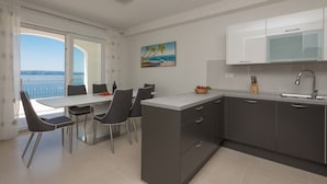 Une cuisine moderne avec des meubles de couleur sombre, un plan de travail blanc et une vue sur la mer grâce à une grande fenêtre.