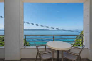Ein Balkon mit rundem Tisch und Stühlen, mit Blick auf das klare, blaue Meer und ferne Berge.