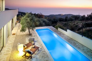 A swimming pool with a view of the sea at sunset, surrounded by stone tiles and a small seating area with a table and chairs. - Villa Tres Chic (Makarska)