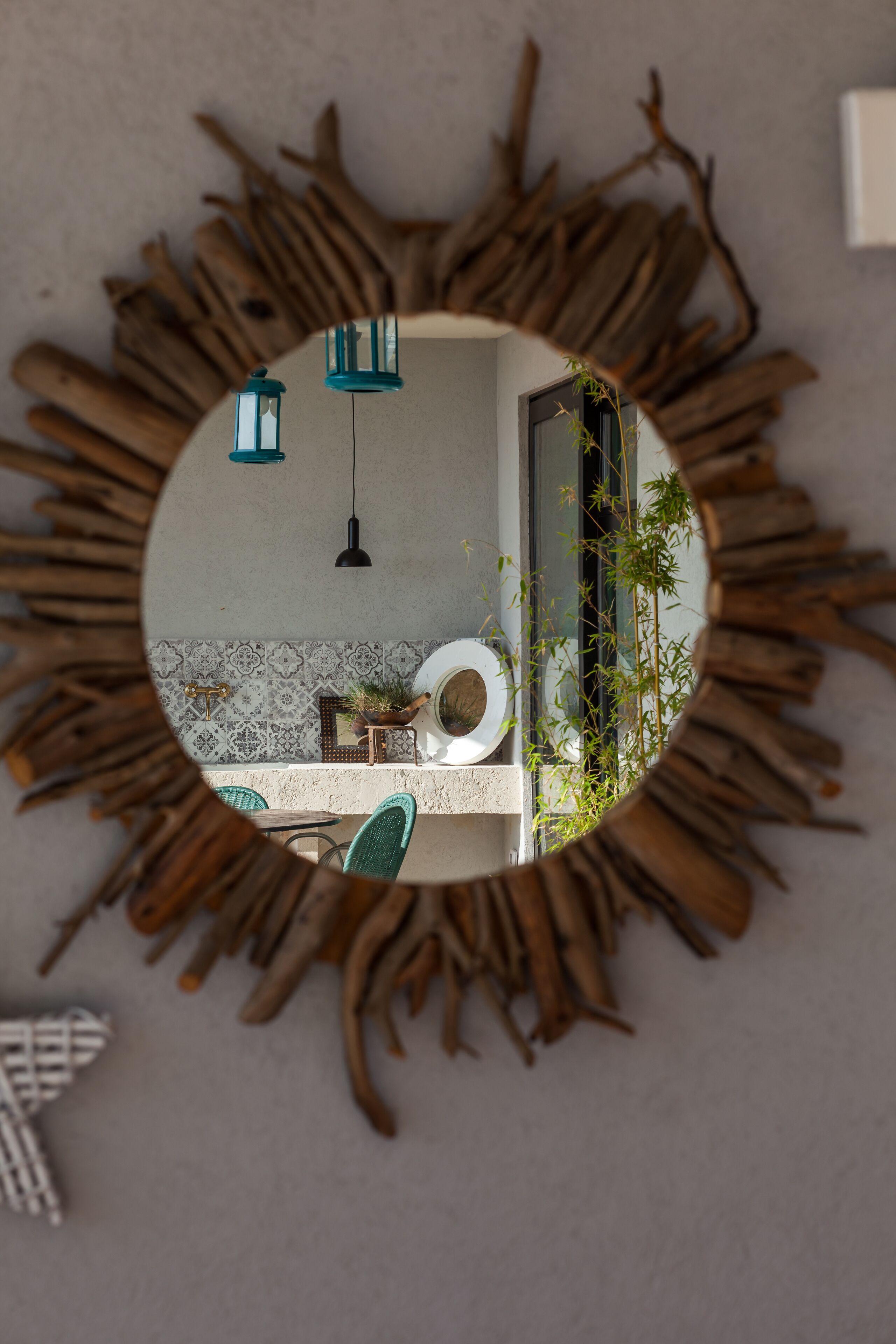 Un miroir rond, doté d’un cadre en forme de soleil, reflète l’intérieur d’une salle de bain avec des toilettes, un lavabo et des luminaires suspendus.