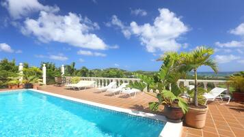 A swimming pool with lounge chairs and potted plants on a terrace with a view of the landscape.