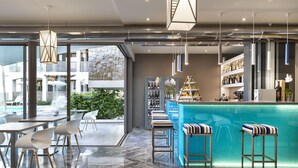 Un espace bar moderne avec un comptoir bleu, des tabourets de bar blancs et une vue sur une piscine à l’extérieur.