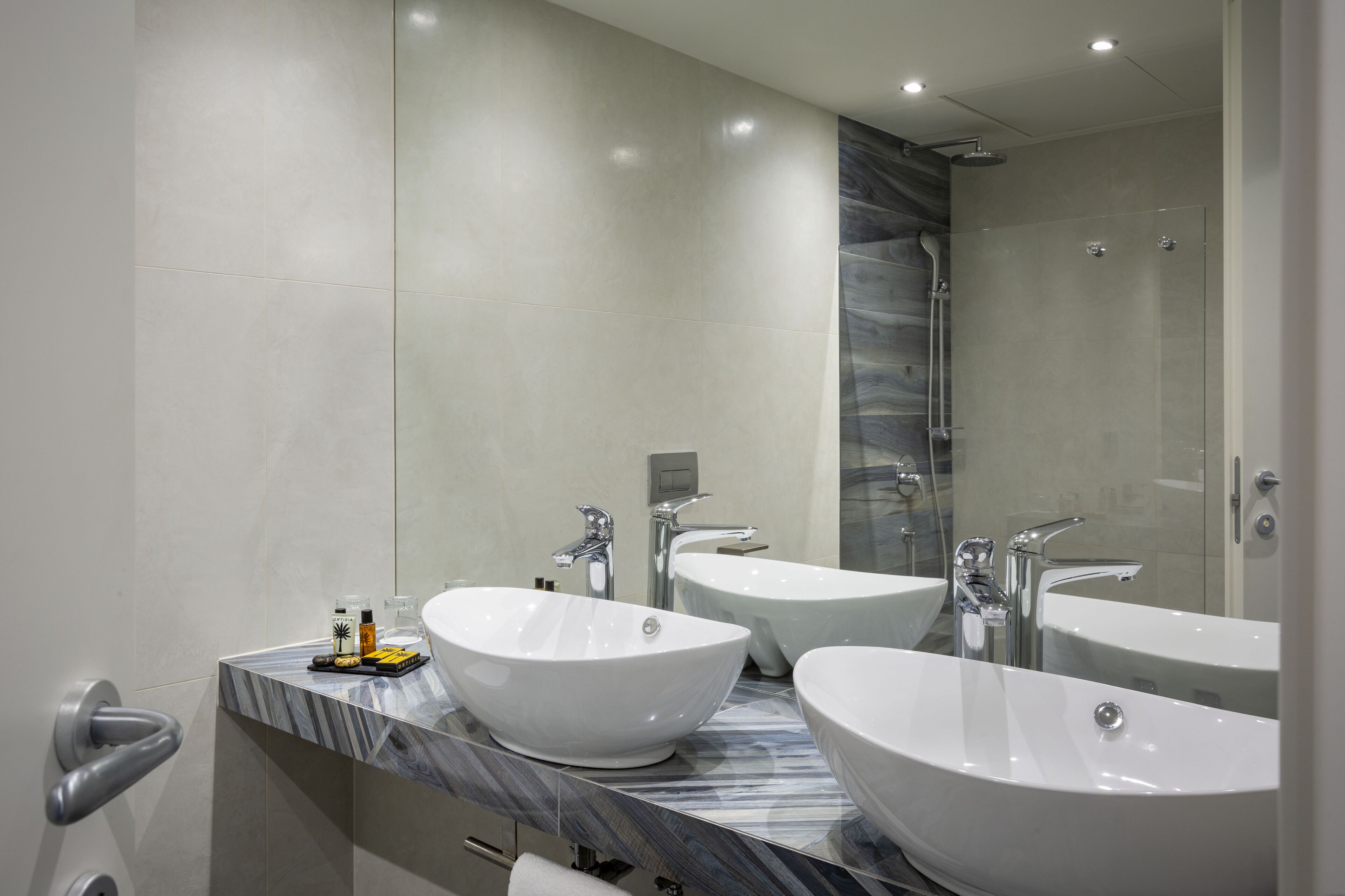 A modern bathroom with two large white sinks, a marble countertop, and a large mirror.